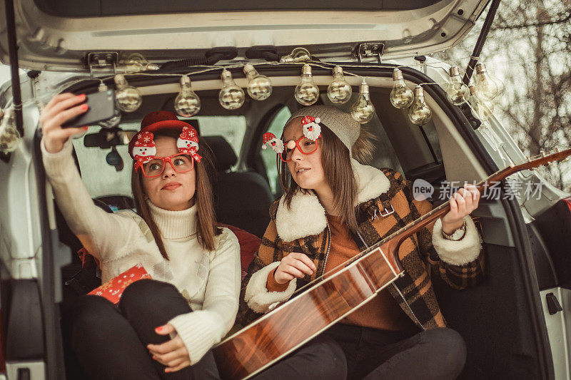 Two women in nature celebrate the new year - Two women in nature celebrate the new year - Two young women celebrate the new year by giving gifts, playing guitar and laugh out - Happy people .两个年轻女性在她们的车里庆祝新年，她们送礼物，弹吉他，放声大笑